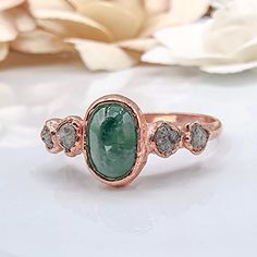 a close up of a ring with a green stone and diamonds on the bottom, surrounded by flowers