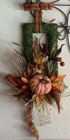 a decorative fall wreath hangs on the wall next to a metal frame with a cross hanging from it