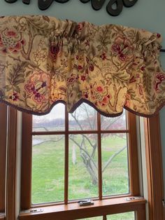 a window with a flowered valance hanging from it's side in front of a green field