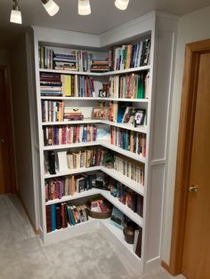 a corner book shelf filled with lots of books on top of white shelving units