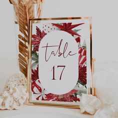 a table number with red flowers and greenery in the center is surrounded by seashells