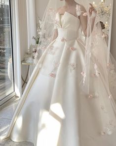 a woman in a white wedding dress standing next to a window with flowers on it