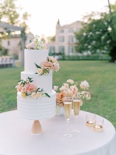 a white wedding cake with flowers on top and two champagne flutes in the foreground