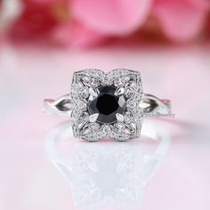 a black and white diamond ring on top of a table with pink flowers in the background