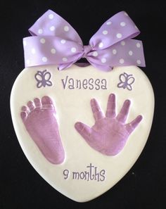 a heart shaped plaque with two handprints and a purple bow on the front