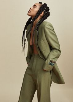 a woman with dreadlocks wearing a green suit and matching pants is looking off to the side