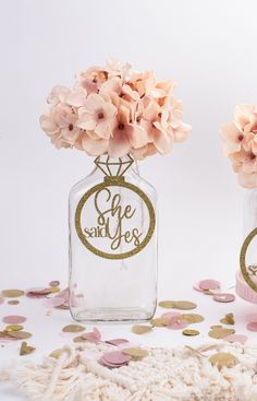 two glass vases with flowers in them on a white surface and confetti scattered around