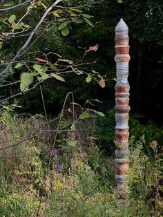 there is a very tall pole made out of ceramic tiles in the grass and trees