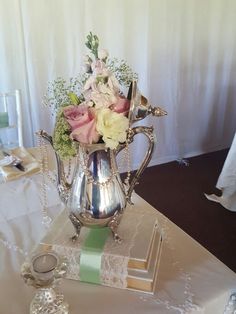 a silver tea pot with flowers in it on top of a white table cloth covered table