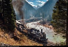 an old train is traveling down the tracks near some trees and mountains in the background