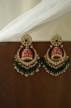 These chandbali earrings feature an opulent design with rich colors. The top stud is a floral design, dangling from it is a heavily encrusted jhumka. The  lower chandbali is an arresting unit embellished with green stones and pearls Closure - Push Back Style Tip - This design is a perfect amalgam of poetic romance and the surrealism of fairy tales. These designs remind us of clear starlit skies, magic and all the poems about love and passion. These designs are perfect for someone who wishes to a Kundan Chandbali Earrings, Red And Green Earrings, Green Kundan Earrings, Sabyasachi Jewellery Jhumkas, Kundan Jhumka Earrings Gold, Single Stone Studs Earrings Gold India, Chaandbaali Earrings Gold, Green Jhumka Earrings, Kundan Chandbali Earrings Gold