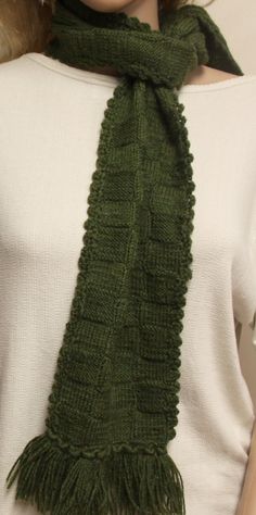 a woman wearing a green knitted scarf with tassels on her neck and white top