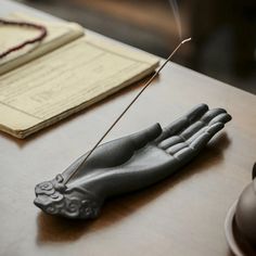 a hand holding a stick on top of a wooden table next to a cup and saucer