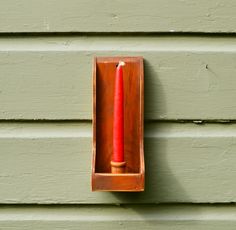 a red candle in a wooden holder on the side of a green building with siding