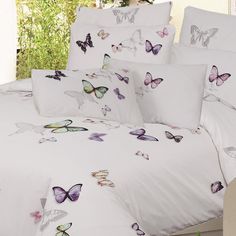 a bed covered in white sheets and pillows with colorful butterflies on the comforter cover