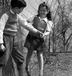 two young children standing next to each other near a tree