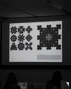 people are sitting in front of a projector screen with black and white designs on it