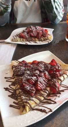 two white plates topped with chocolate covered crepes and strawberries on top of each other