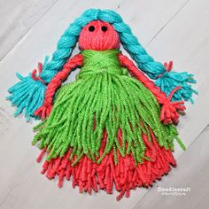 a handmade doll with blue hair and green dress sitting on top of a wooden floor