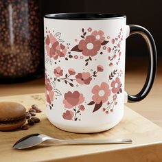 a white and pink coffee mug sitting on top of a wooden table next to a spoon