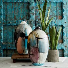 two vases sitting next to each other with plants in front of them on a table