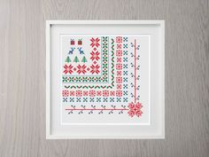 a cross - stitch pattern in a white frame on a wooden surface, with red and green designs