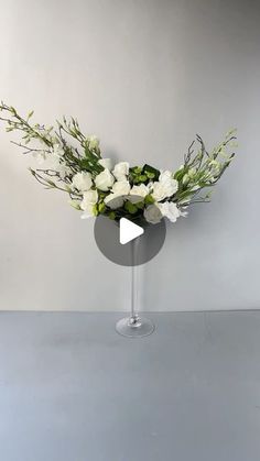 a vase filled with white flowers sitting on top of a gray table next to a wall