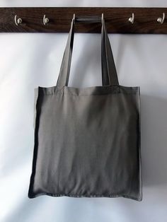 a gray bag hanging from a wooden coat hook on a white wall with black handles