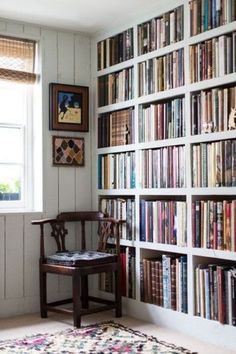 a room filled with lots of books on top of a white book shelf next to a window