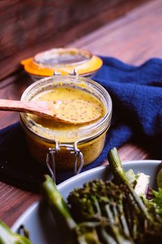 there is a bowl of broccoli next to a jar of mustard on the table