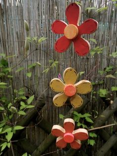 three red and yellow flowers are hanging from a wire in front of a bamboo fence