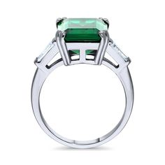 This 3-stone ring makes the ultimate statement with its stunning brilliance and regal high setting. Make a statement and turn heads with this one of a kind beauty. Crafted with fine 925 sterling silver, rhodium plated, nickel free. Main stone features 8.5 carat simulated emerald emerald cut cubic zirconia (14mm x 10mm) in prong setting. Accented with 0.24 ct.tw step-cut trapezoid CZ (5mm x 3mm x 2mm) in bar setting. Ring measures 7.7mm in height. Band measures 2mm in width. Adds a bling on your Jewlery Rings, Cocktail Fashion, Bar Setting, Regal Elegance, Crazy Rich, Accesories Jewelry, 3 Stone Rings, Semi Precious Gems, Stone Feature