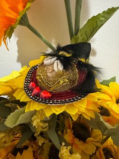 a sunflower with a hat on it sitting in front of a white wall and yellow flowers