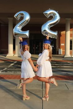 two girls in graduation attire hold up large silver numbers that spell out the number 22