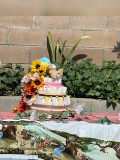 a cake with sunflowers and other decorations sits on a table in front of a brick wall