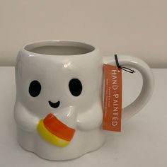 a white mug with a candy corn on it and a tag hanging from the handle