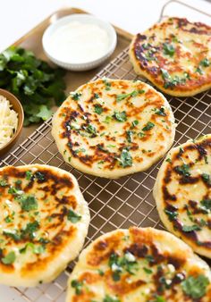 several flat bread pizzas on a cooling rack with some dipping sauce and parsley