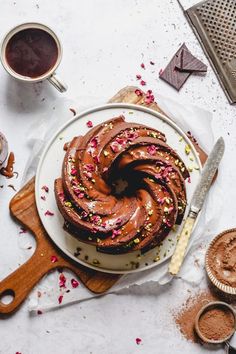 a chocolate bundt cake with sprinkles on a plate next to two cups of coffee