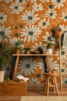 an orange wall with white daisies on it and a wooden stool next to the table