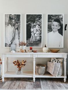 three pictures hang on the wall above a white console table with baskets and vases