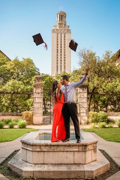 a man and woman in graduation gowns standing on a fountain with their arms around each other