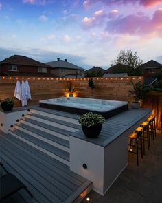 a hot tub sitting on top of a patio next to a wooden fence with string lights