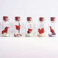 four glass bottles with red origami birds in them, one is empty and the other has flowers inside