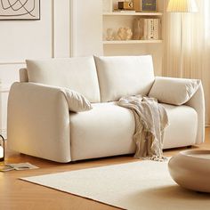 a white couch sitting on top of a hard wood floor next to a table and lamp