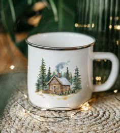 a mug with a cabin on it sitting on a table next to a potted plant