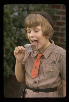 a young boy in uniform eating a piece of food with his mouth open and tongue out