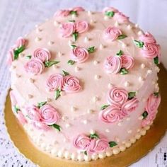 a cake with pink frosting and roses on it is sitting on a doily