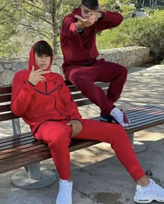 two young men sitting on a park bench wearing matching tracksuits and hoodies