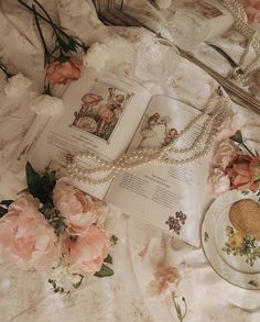 an open book on a bed with flowers and pearls