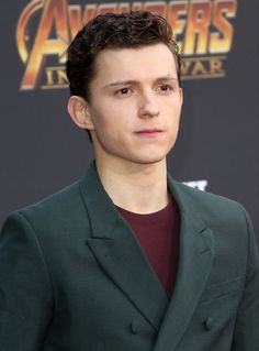 the young man is wearing a suit and posing for a photo in front of an avengers logo